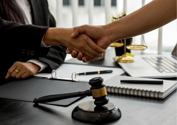 2 people shaking hands over a desk that has papers and a gavel