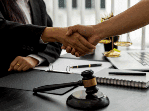 2 people shaking hands over a desk that has papers and a gavel