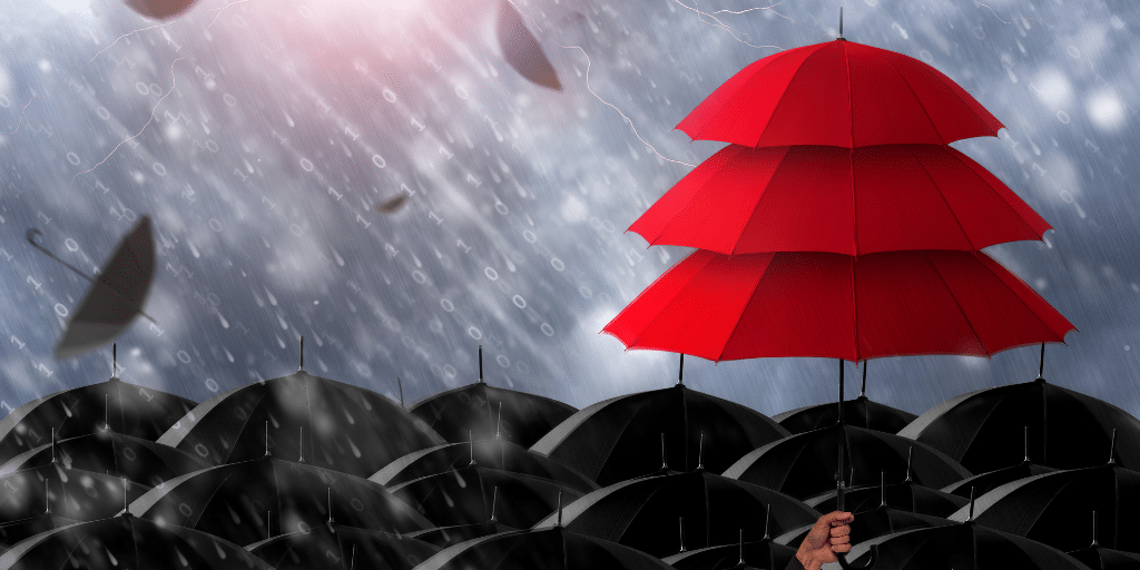 Lots of black umbrellas grouped together with rain coming down over the top. There are 3 red umbrellas stacked on top of each other off to the right of the image over the black umbrellas.