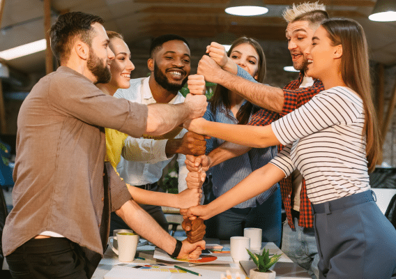 Group of six adults all piling their hands on top of each other's to show teamwork