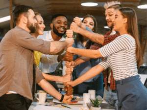 Group of six adults all piling their hands on top of each other's to show teamwork