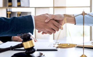 Two people shaking hands. Gavel and justice scale in the foreground.