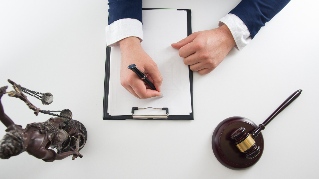 Image of a business professional writing on a blank paper. There is a justice statue and a gavel off to the side.