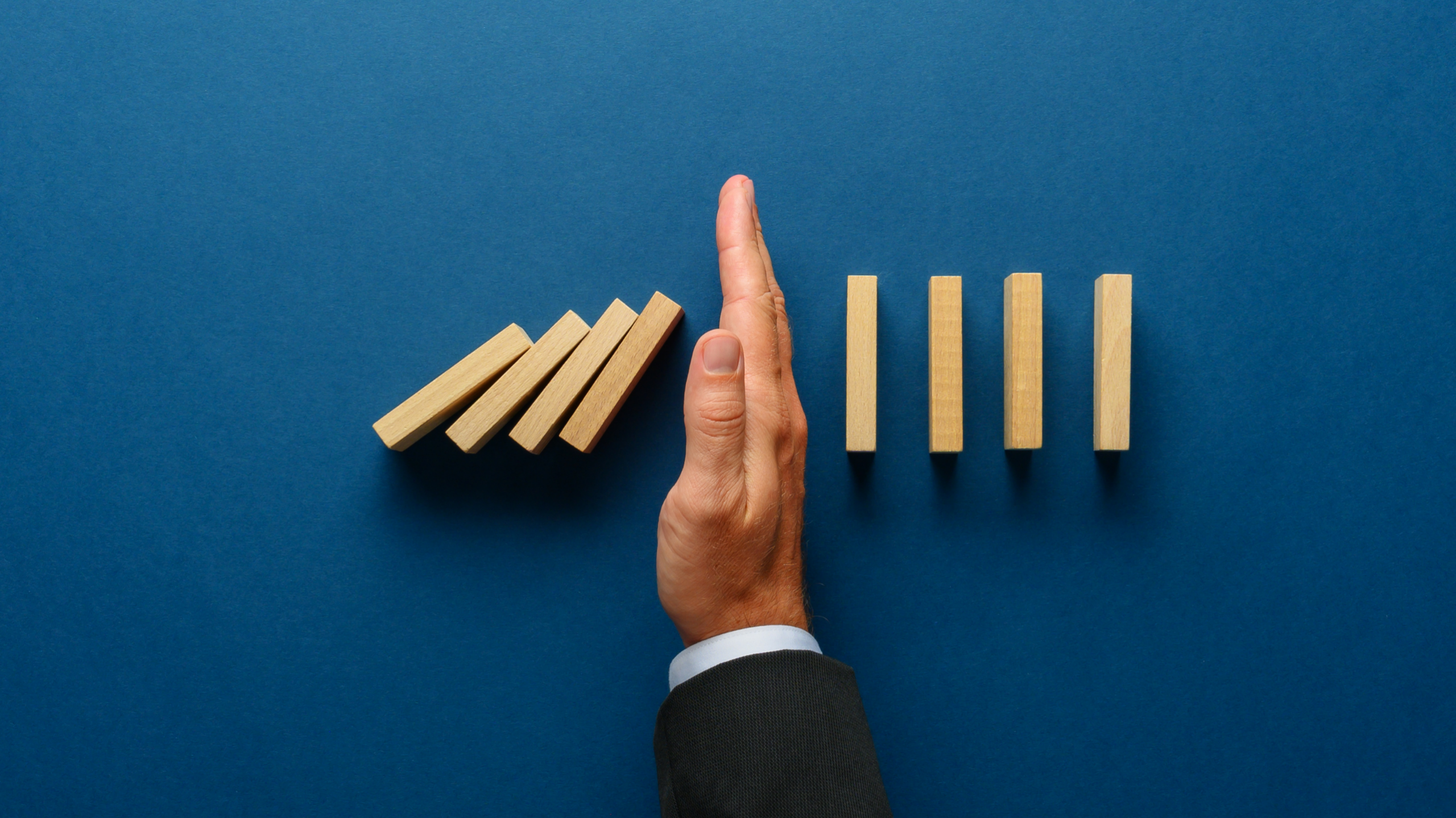 Persons hand stopping dominoes from falling