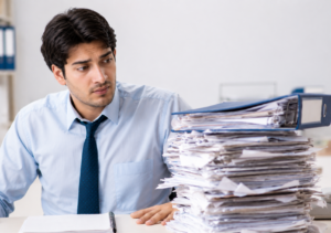 Man sitting at the desk looking overwhelmed at a large stack of papers