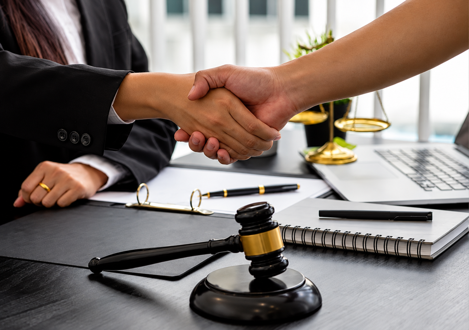 2 people shaking hands over a desk that has papers and a gavel