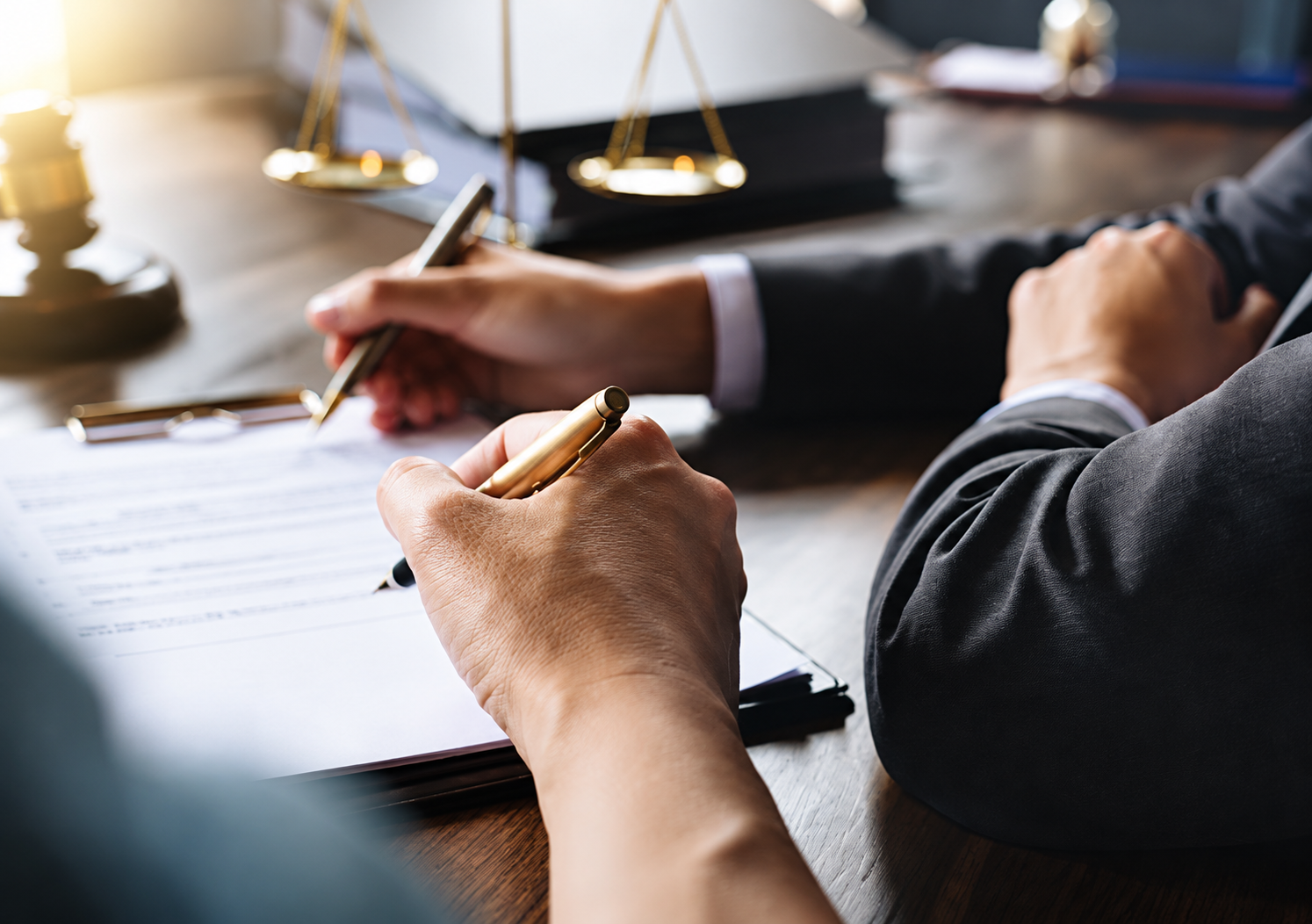 Two people signing a document. Justice scale in the background.